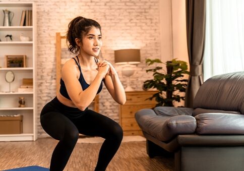 Young fit Asian woman working out at home. Beautiful female athlete training for legs muscles with squats exercise move.